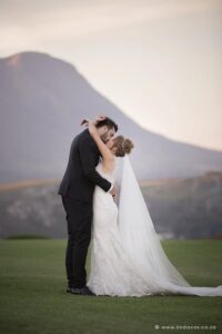 Bride and groom kissing with scenic views of mountains on beautiful green grass